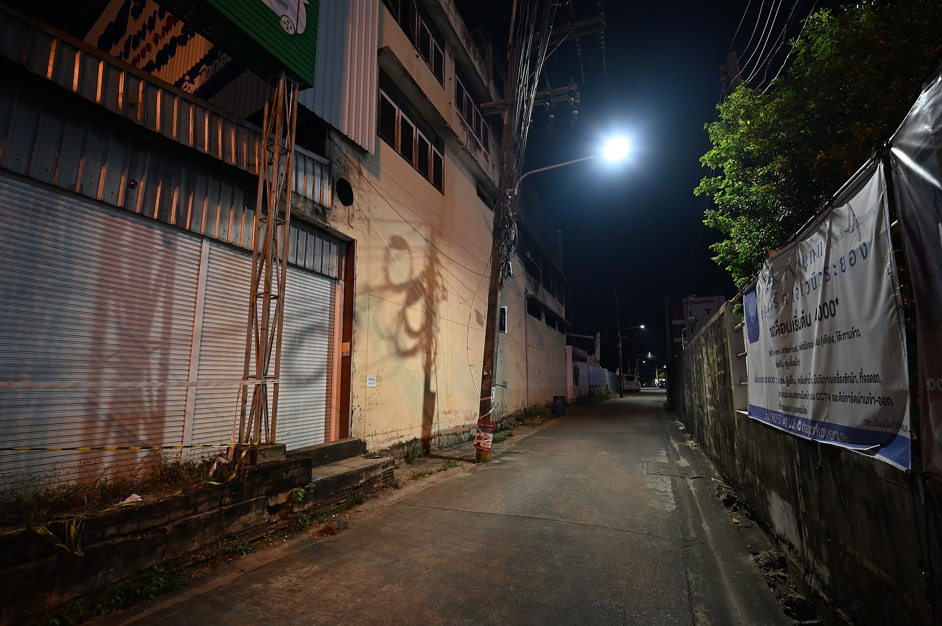 Fachadas de comercios pequeños con las persianas bajadas en un callejón de noche, iluminado por una única lámpara